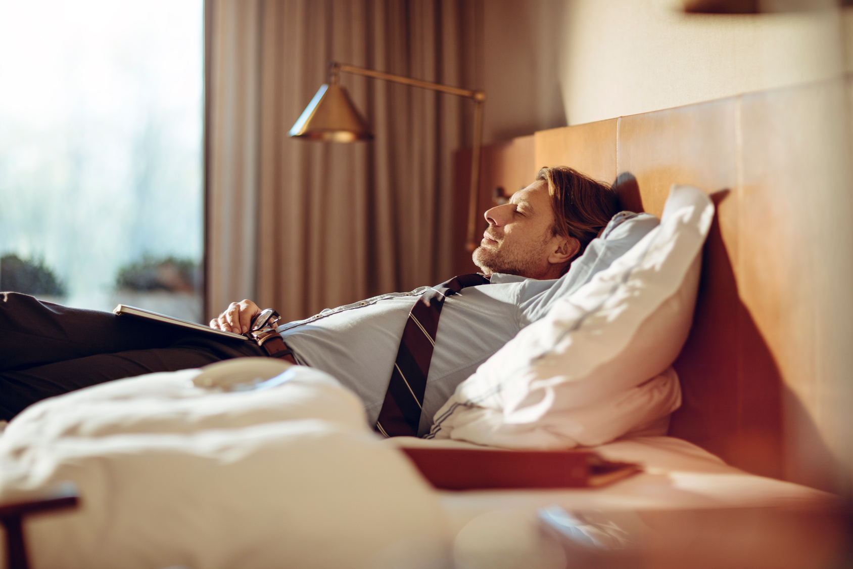 Mature businessman lying down in a bed in a hotel room
